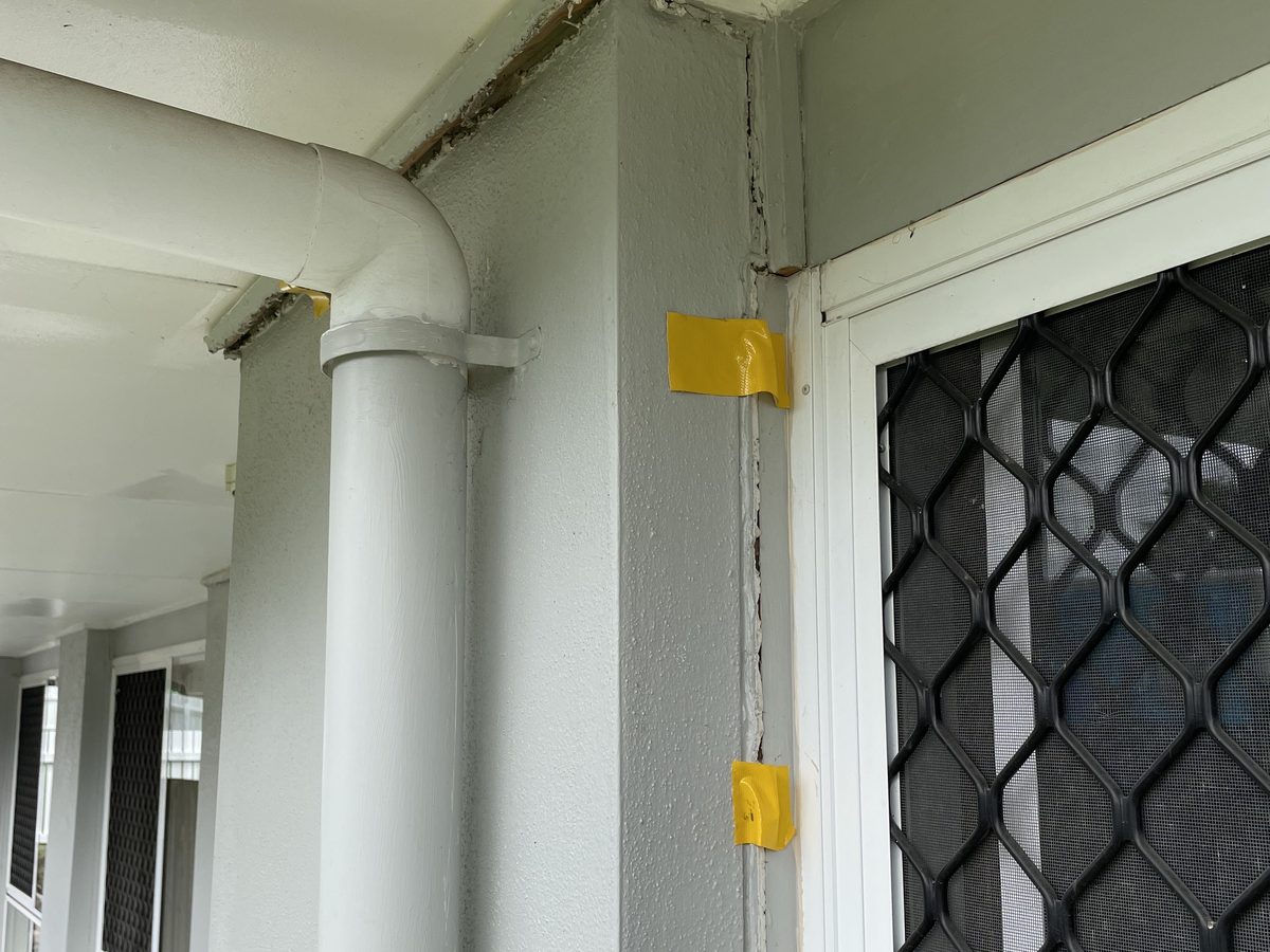 After: the same crack closed to a thin line, the yellow gauge tape now buckled where the gap has shut