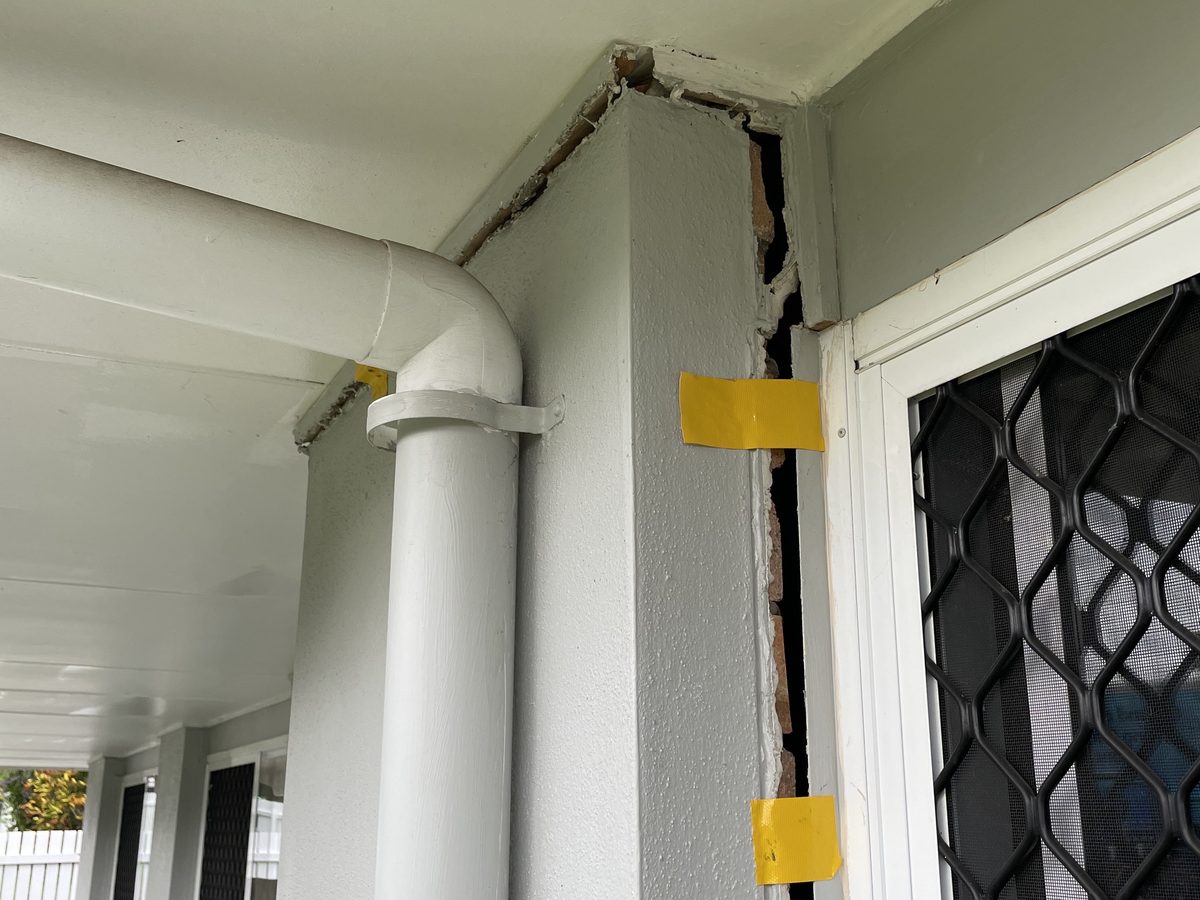 Before: a crack wide enough to see through, running down a rendered wall beside a door frame, with yellow gauge tape stretched across it