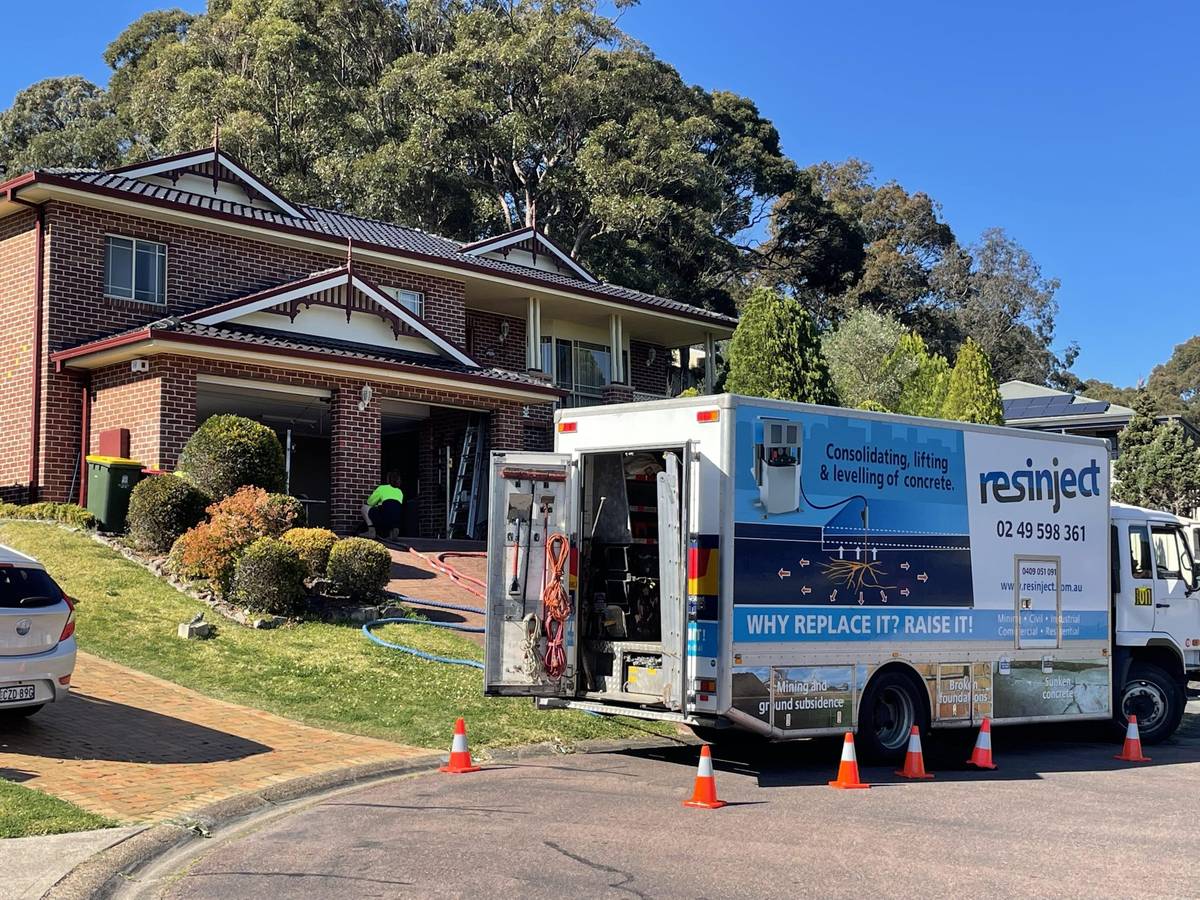 Resinject truck set up on the street outside a two-storey brick home, hoses running to the injection points